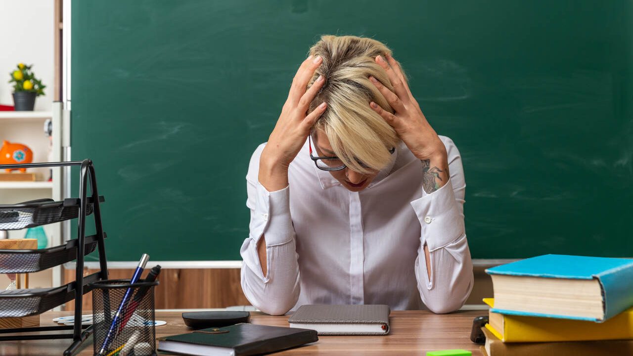 Professora em sala de aula com as mãos na cabeça preocupada por ser uma das profissões menos valorizadas