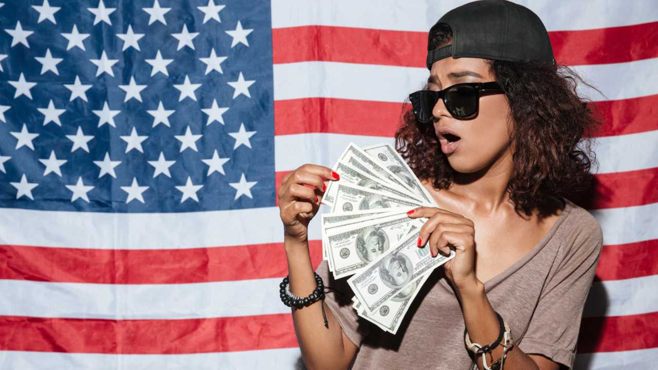 Garota na frente da bandeira dos EUA com salário mínimo em dólar na mão