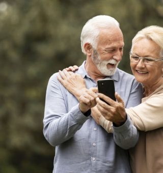 Idosos abraçados ao ar livre usando celular para ver a tabela de reajuste de aposentados